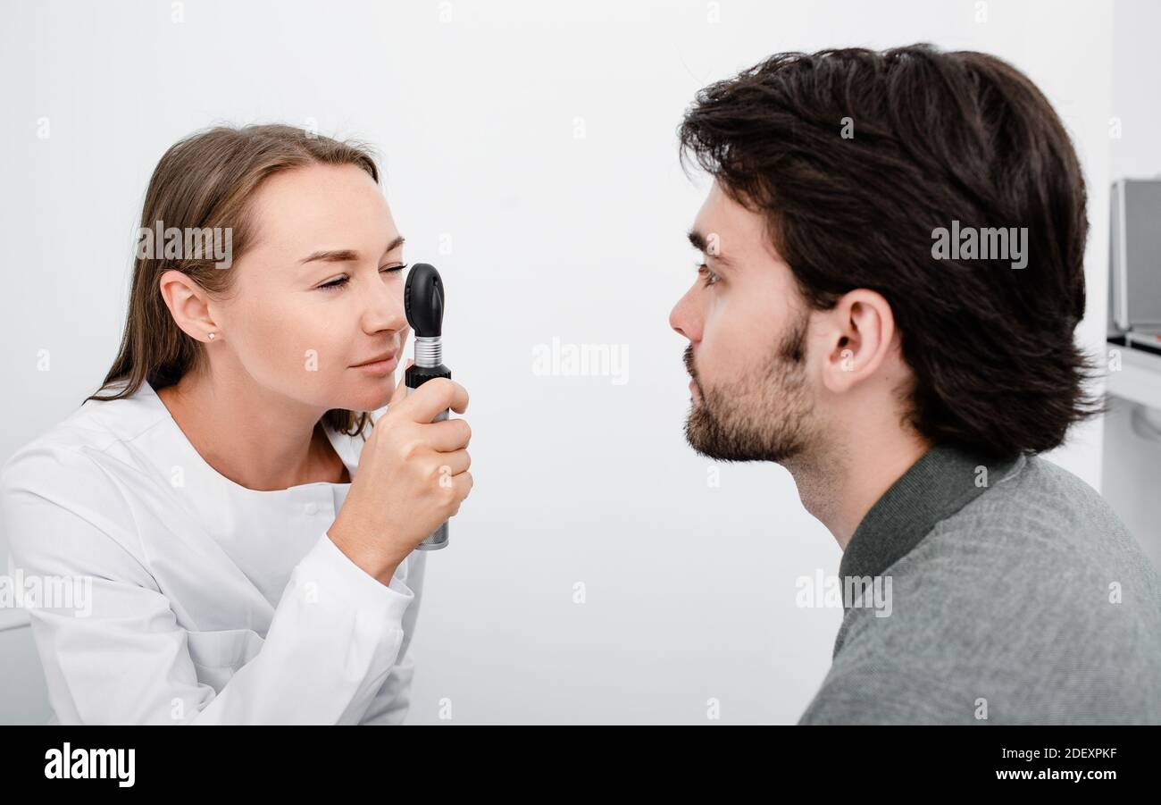 Donna optometista che controlla gli occhi di un uomo con un oftalmoscopio. Esame degli occhi di persone adulte Foto Stock