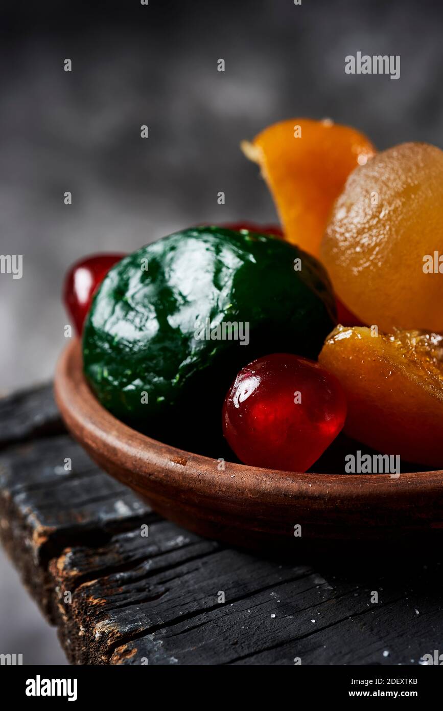 primo piano di alcuni appetitosi frutti canditi spagnoli, come l'arancia, la pera, la prugna o le ciliegie di maraschino, tipicamente consumate il natale, su un rustico gr scuro Foto Stock