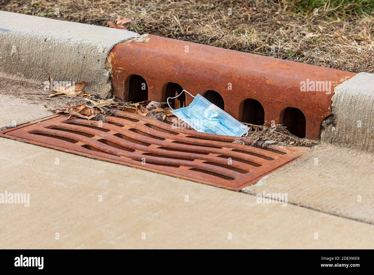 Closeup di maschera chirurgica viso scartato nella rete fognaria tempesta scarico. Concetto di inquinamento pandemico del coronavirus Covid-19 e smaltimento sicuro della copertura del viso Foto Stock