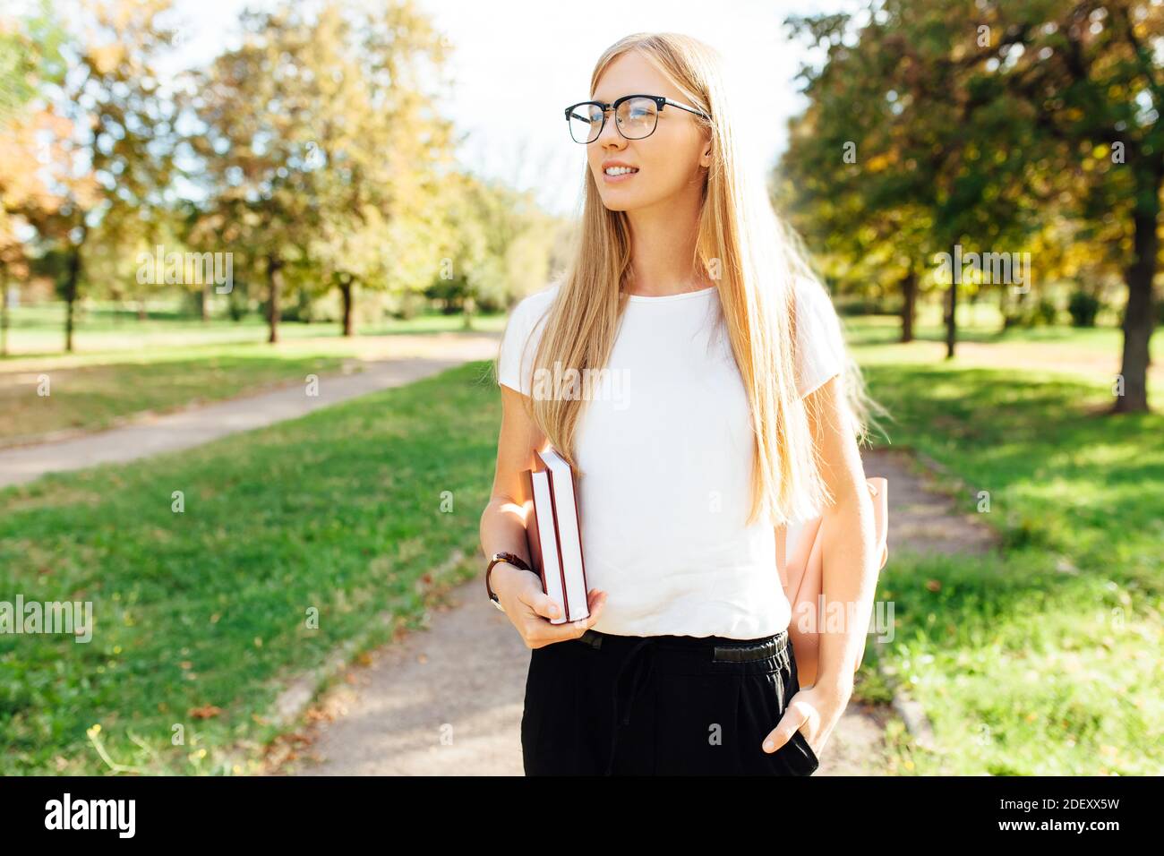 Ritratto di una bella studentessa con occhiali, camminando nel Parco, tenendo libri in mano, riposo dopo classe Foto Stock