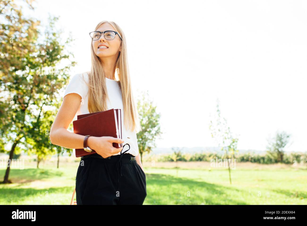 Ritratto di una bella studentessa con occhiali, camminando nel Parco, tenendo libri in mano, riposo dopo classe Foto Stock