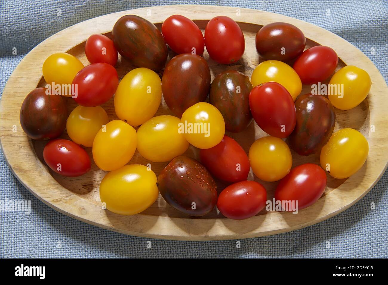 Pomodori ciliegini. Isolato. Varietà colorata di pomodori ciliegini su un piatto di legno. Immagine stock. Foto Stock