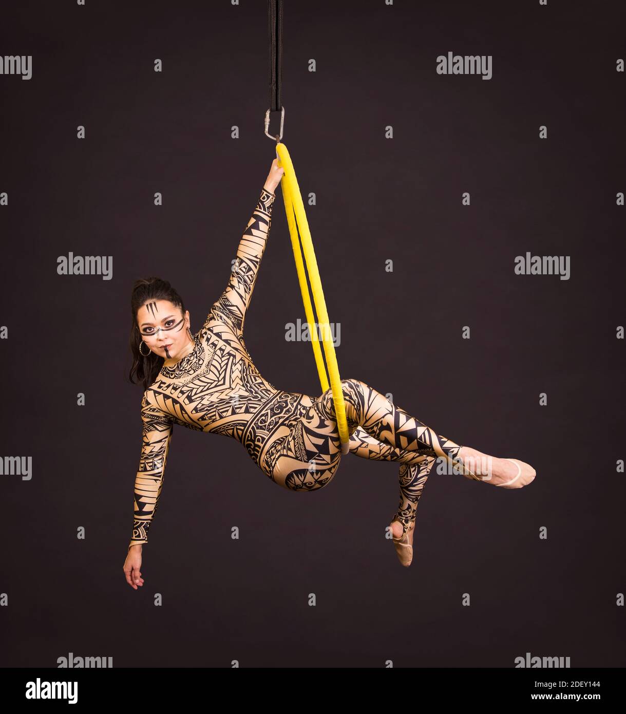 Una giovane donna in tuta con stampa esegue elementi acrobatici nell'anello dell'aria. Riprese in studio su sfondo nero. Foto Stock