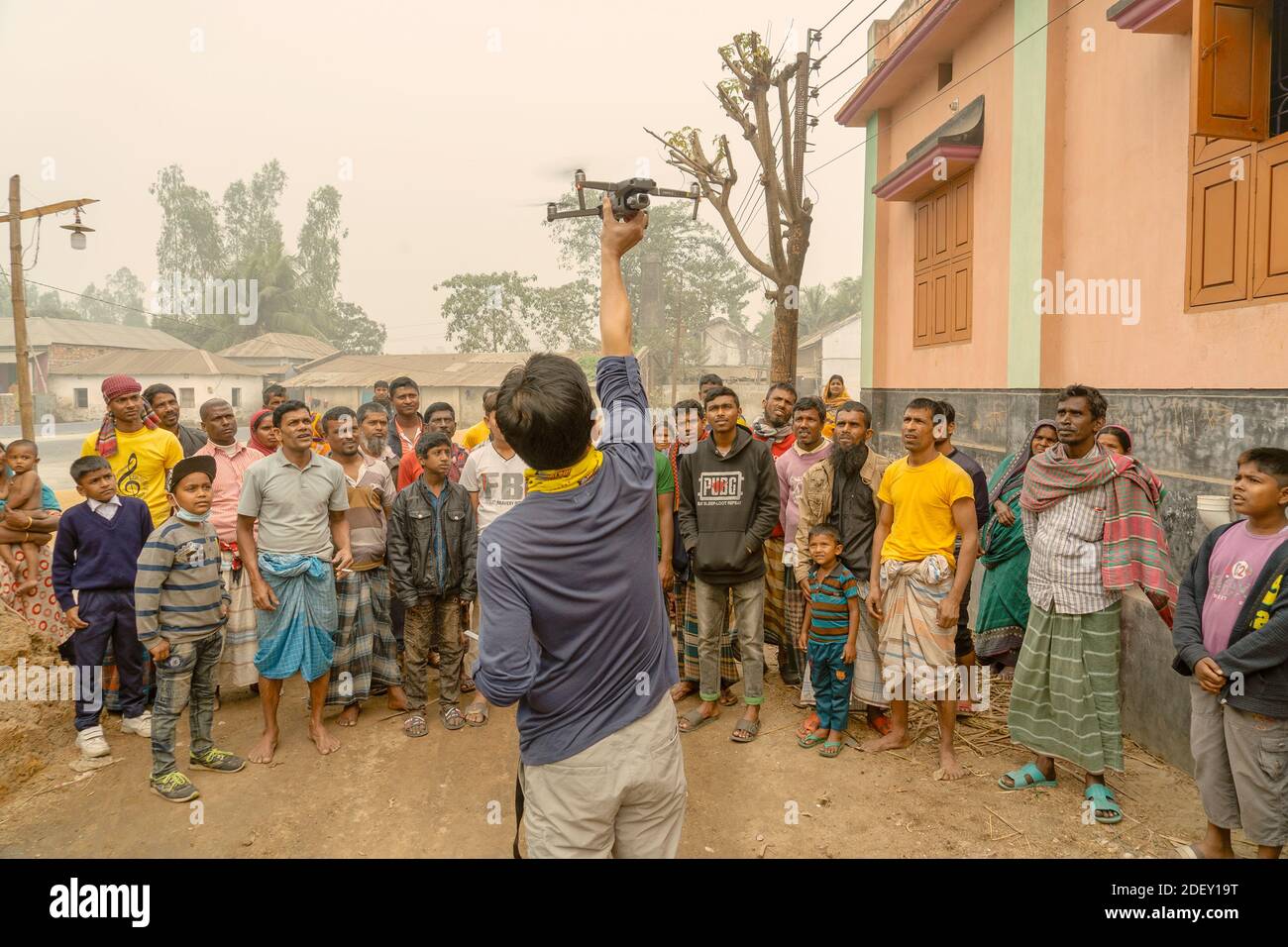 Drone Landing, gente del villaggio del Bangladesh che si trova davanti alla loro casa guardando un drone di atterraggio. Foto Stock