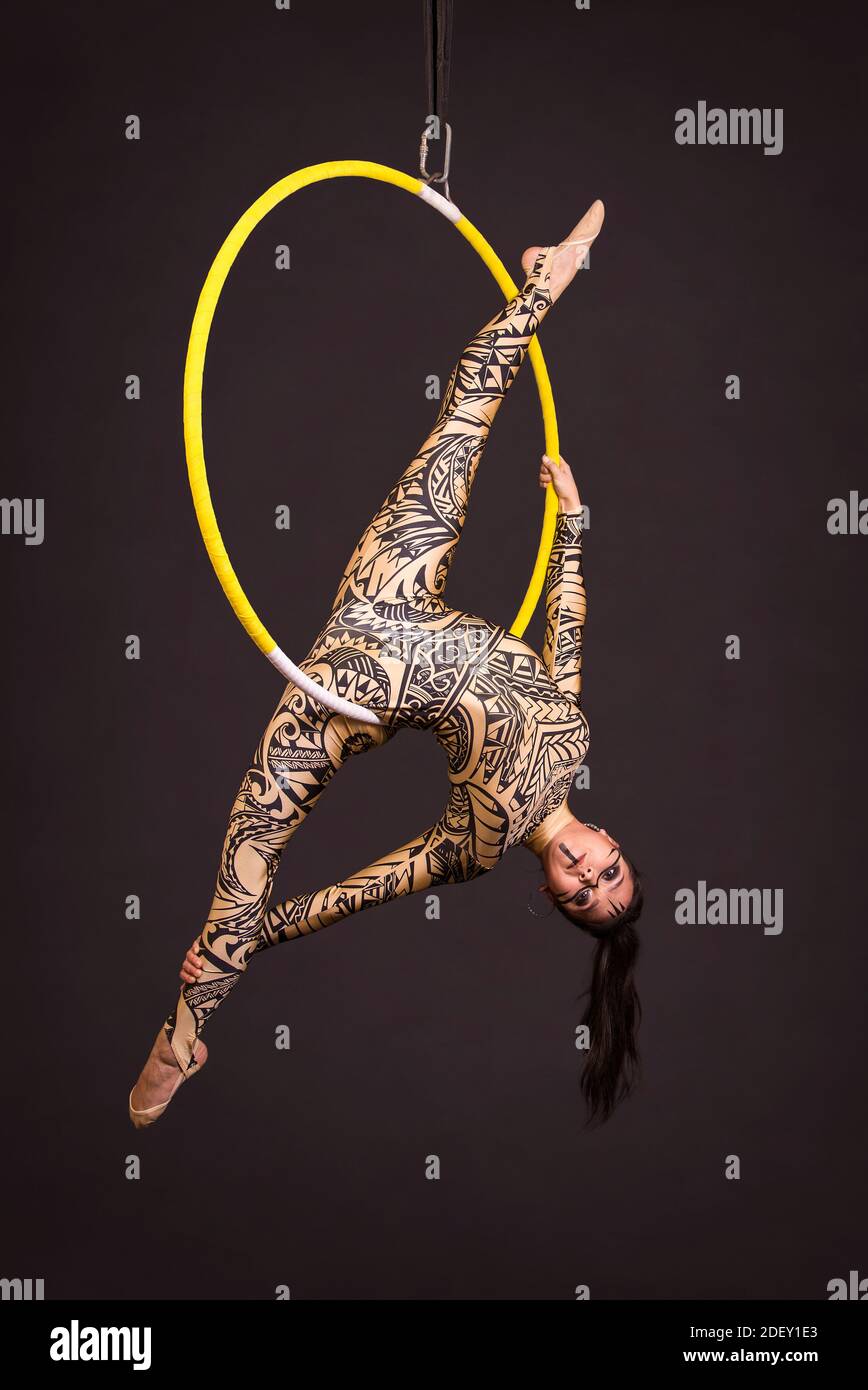 Una giovane donna in tuta con stampa esegue elementi acrobatici nell'anello dell'aria. Riprese in studio su sfondo nero. Foto Stock