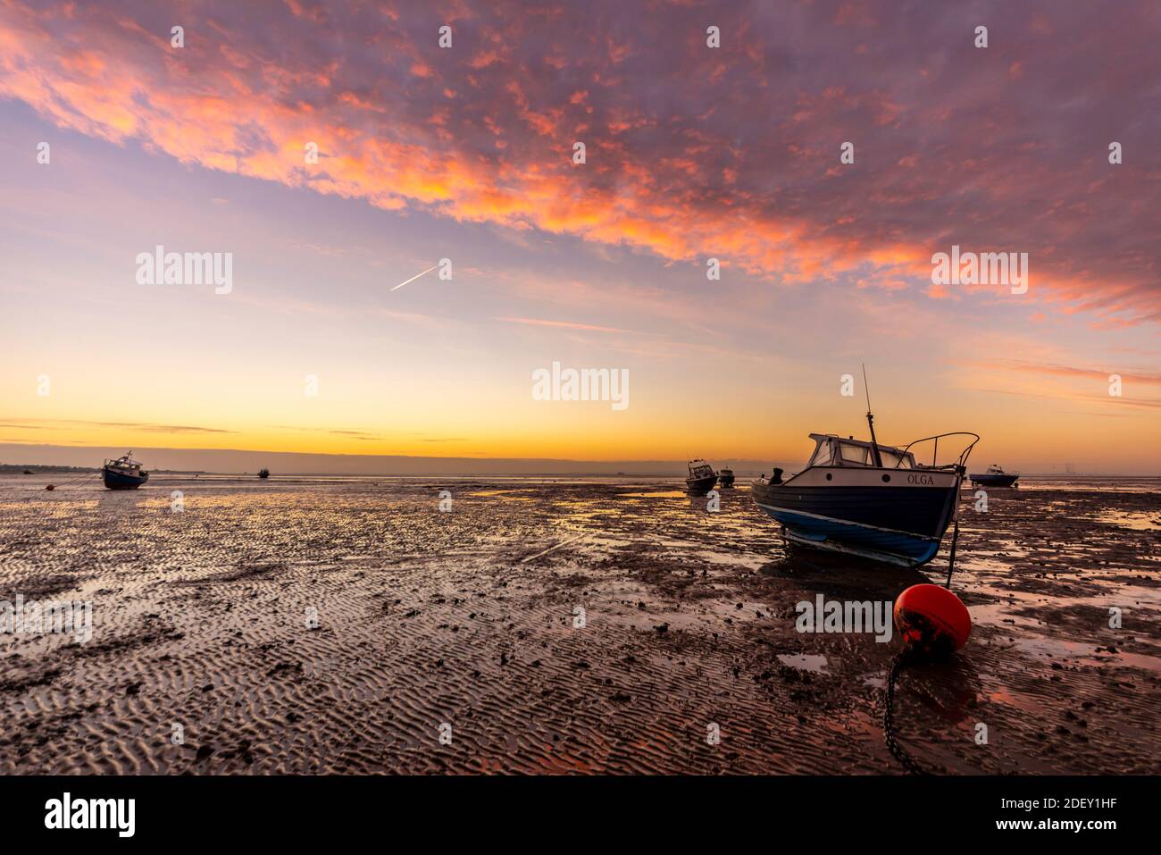 Barche sul fango a bassa marea nel Tamigi estuario ormeggiato al largo di Southend sul mare, Essex, Regno Unito, all'alba con i colori dell'alba che mette in risalto la banca nuvolosa Foto Stock