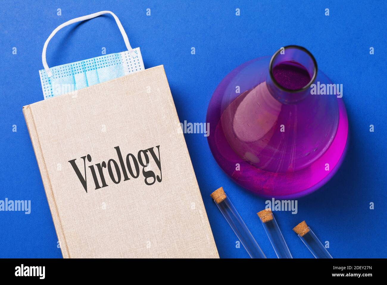 Libro di testo Virology con un segnalibro da una maschera medica e reagenti diversi sulla tabella. Foto Stock