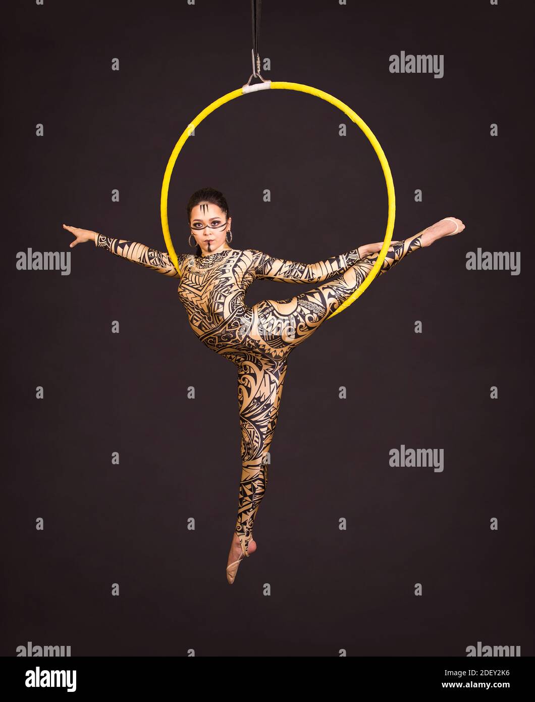 Una giovane donna in tuta con stampa esegue elementi acrobatici nell'anello dell'aria. Riprese in studio su sfondo nero. Foto Stock
