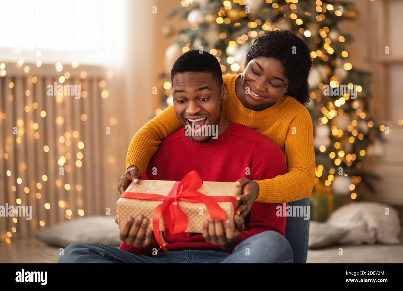 Sorpreso africano americano giovane marito tenere scatola con dono e. nastro rosso Foto Stock