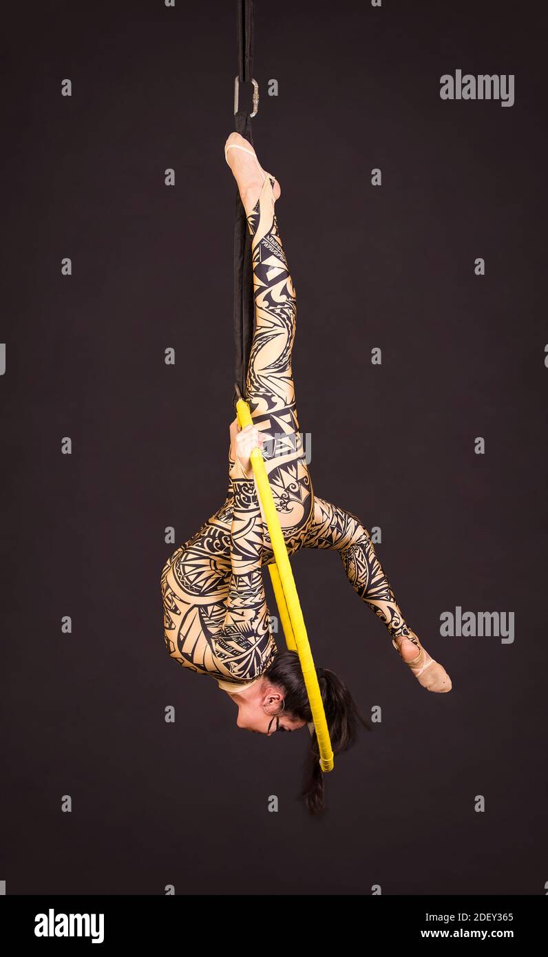 Una giovane donna in tuta con stampa esegue elementi acrobatici nell'anello dell'aria. Riprese in studio su sfondo nero. Foto Stock