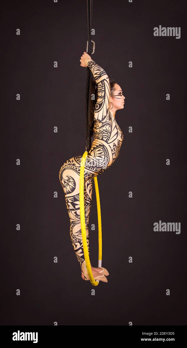 Una giovane donna in tuta con stampa esegue elementi acrobatici nell'anello dell'aria. Riprese in studio su sfondo nero. Foto Stock