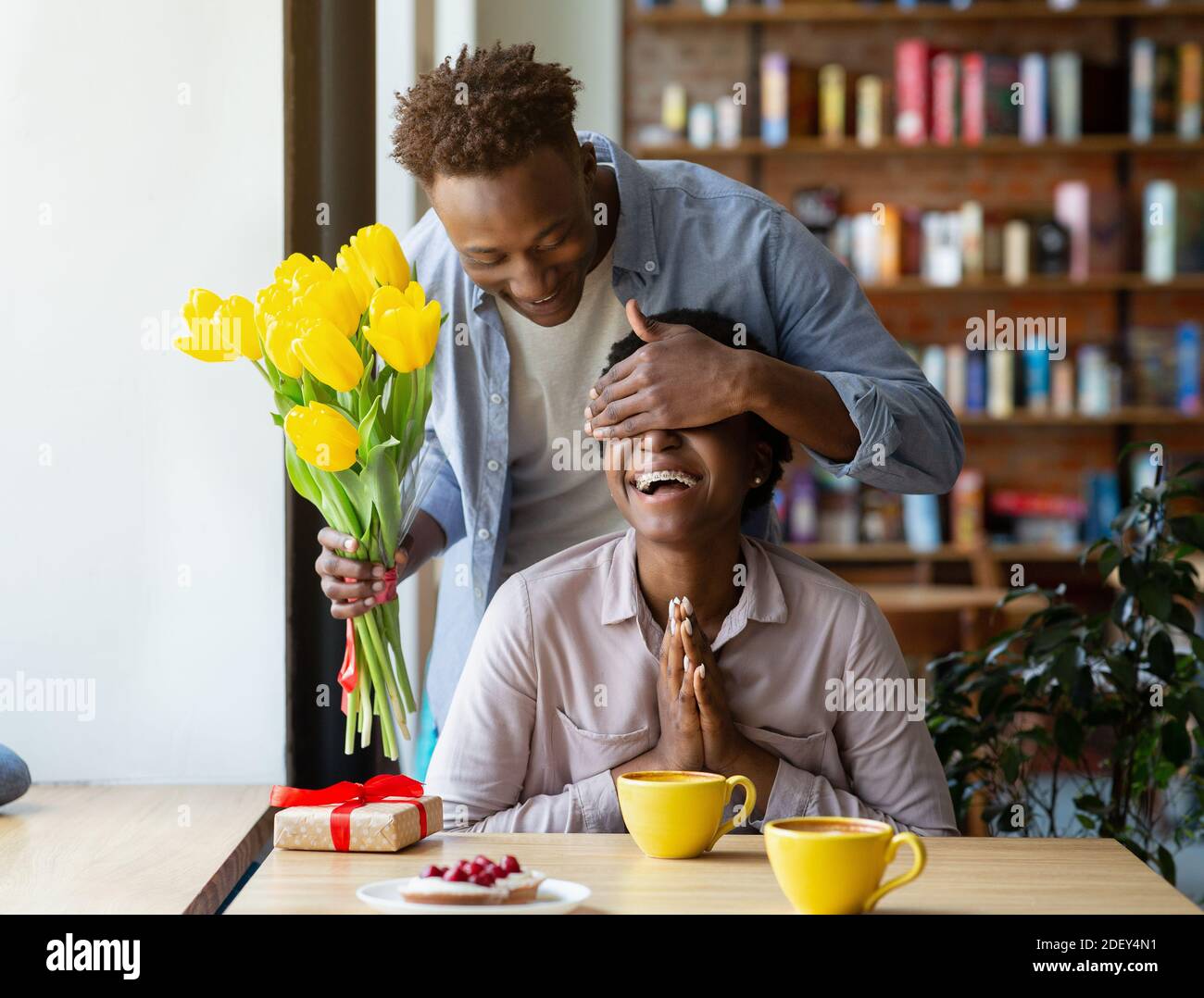 Ragazzo nero amorevole sorprende la sua ragazza con bei tulipani gialli presso la caffetteria Foto Stock