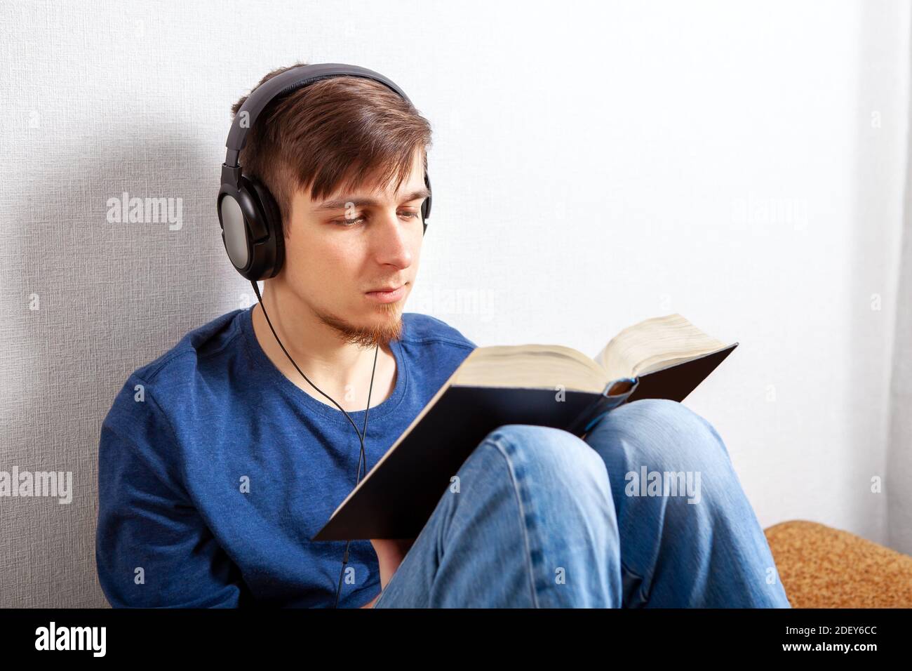 Young Man in Headphones leggere un libro a casa Foto Stock