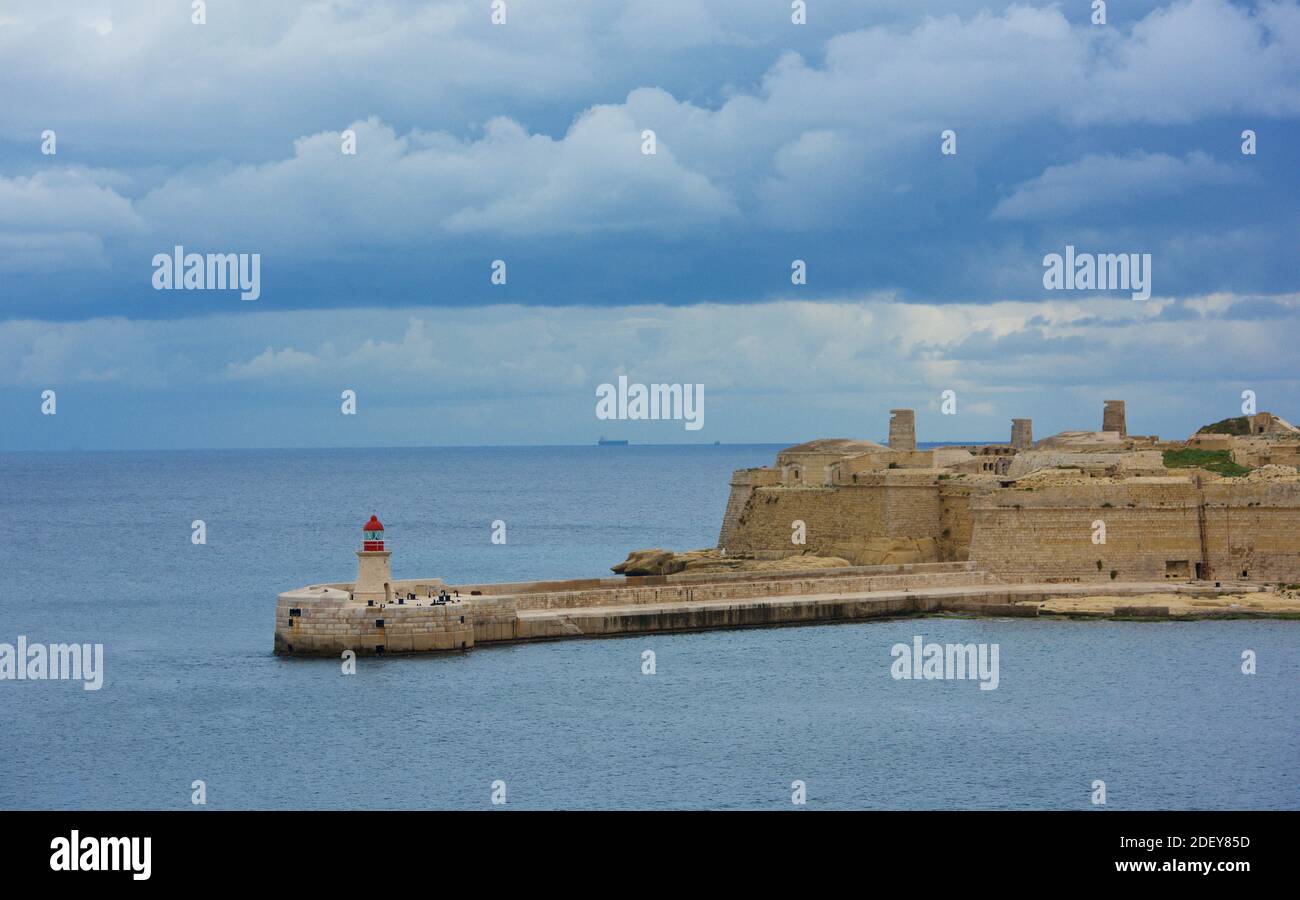 Vista panoramica sul forte Ricasoli con faro in primo piano. Ingresso al Porto di la Valletta, Malta, in una bella giornata con splendide nuvole. Foto Stock