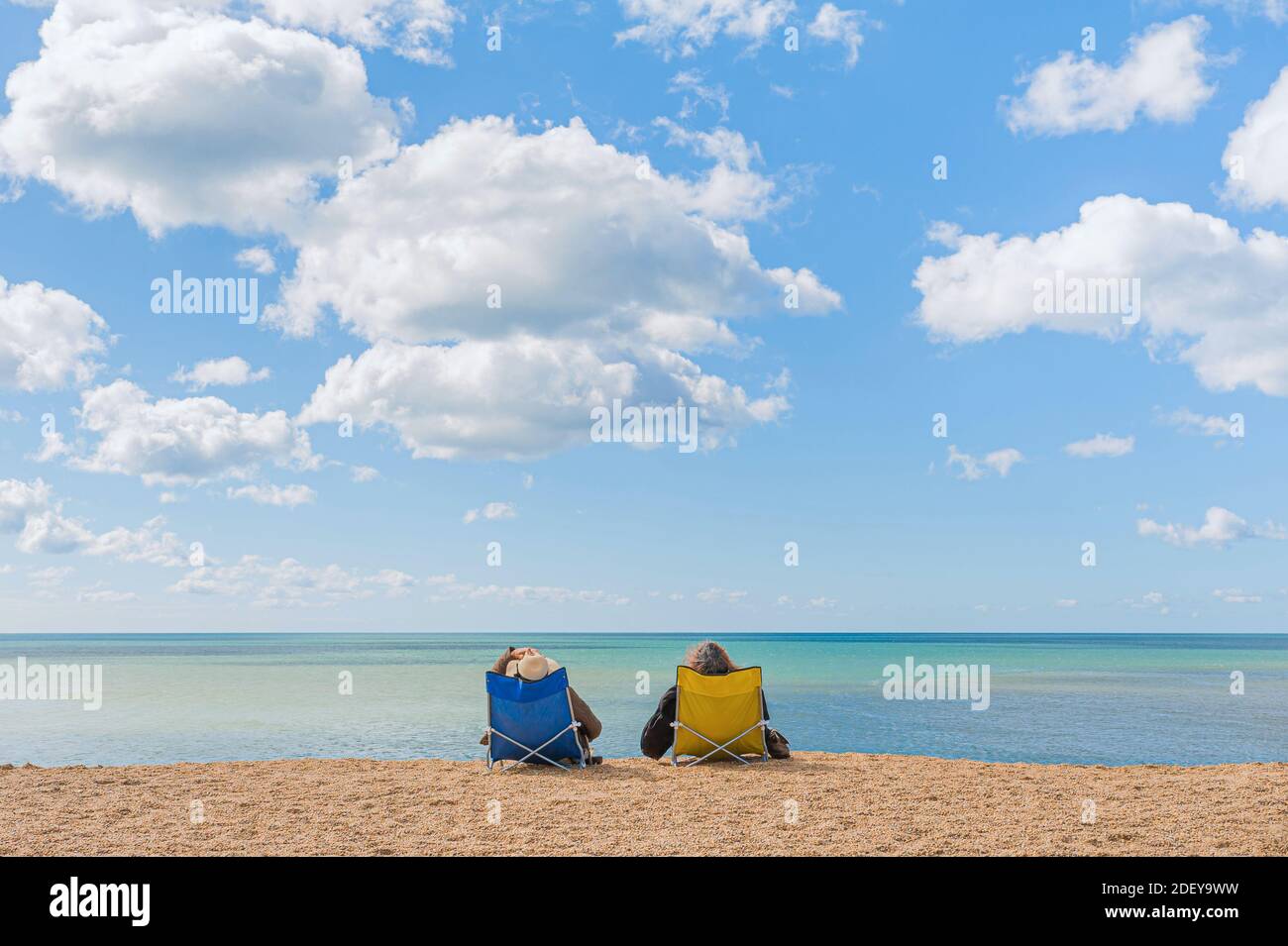 Una coppia comodamente seduta in sedie da spiaggia godendo di una vista indisturbata in acque tranquille e calme del mare. Foto Stock