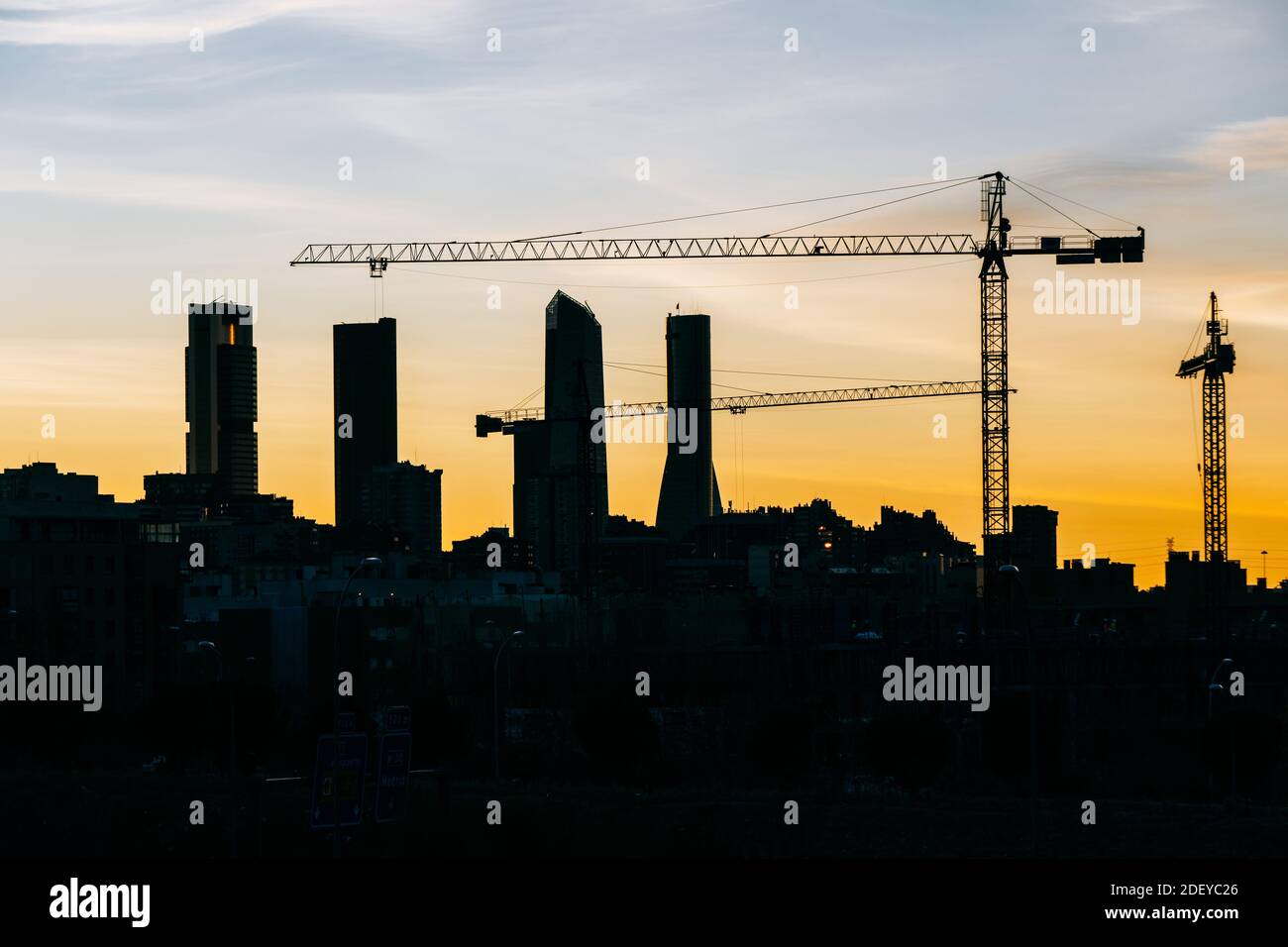 Cuatro Torres Business Area skyline di Madrid al tramonto con gru da costruzione ed edifici residenziali in una vista ravvicinata. Toni arancioni e contast. Foto Stock