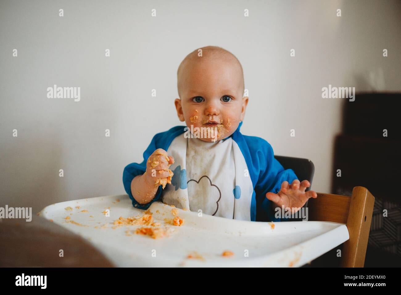 Bambino ragazzo che mangia con le mani facendo un pasticcio con cibo per tutto il viso Foto Stock