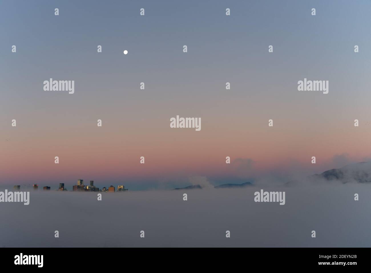 Città nella luna nuvolosa sullo sfondo, Vancouver City grattacieli sopra la nebbia con il sole del mattino creando riflesso falso tramonto lato della luna Foto Stock