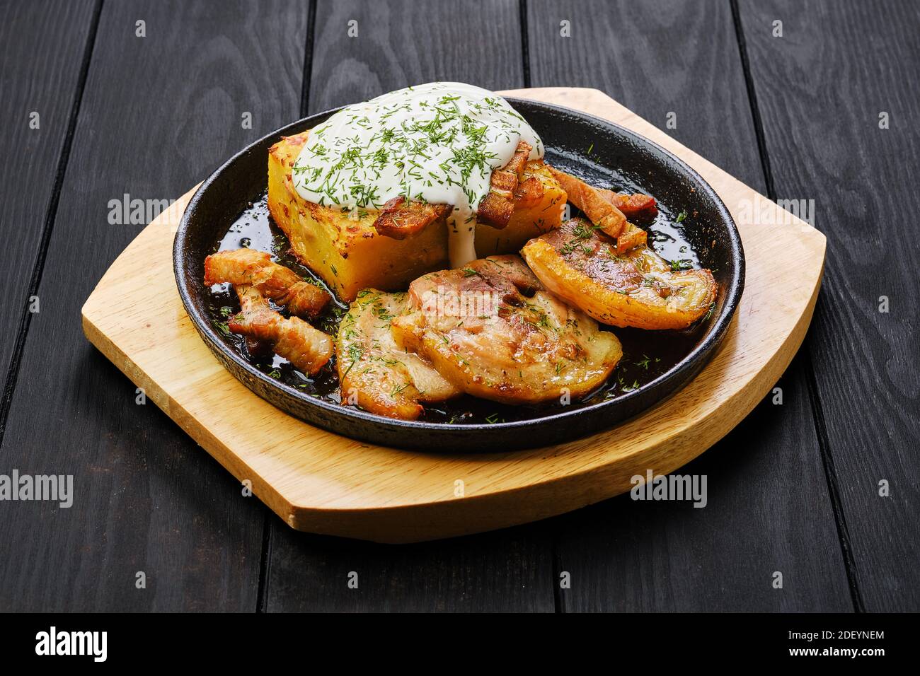 Casseruola di patate con mini fette di pancia di maiale fritte al buio tavolo di legno Foto Stock