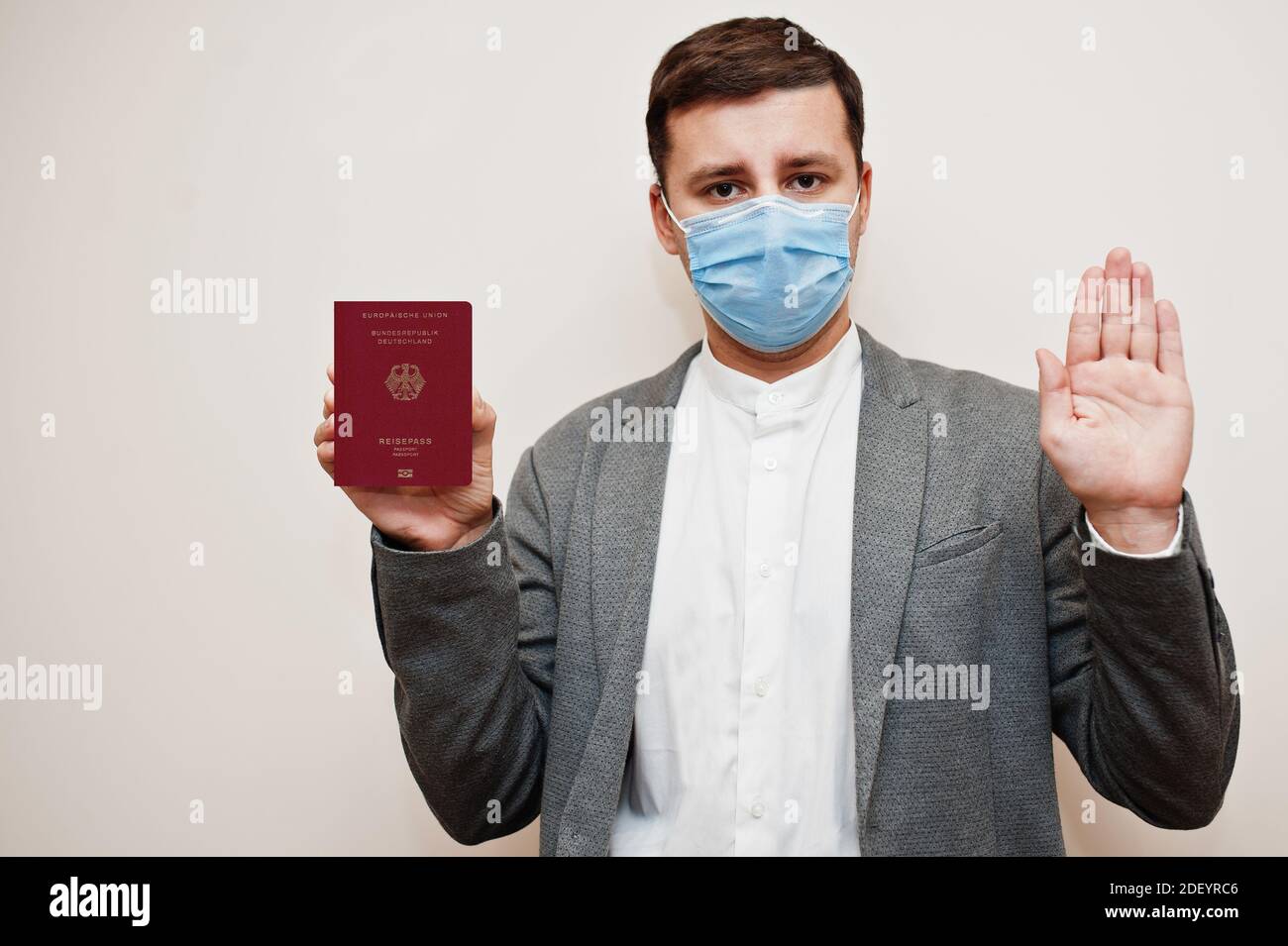 Uomo europeo in abbigliamento formale e maschera facciale, mostra il passaporto tedesco con la mano del segnale di stop. Blocco del coronavirus nel concetto di paese europeo. Foto Stock