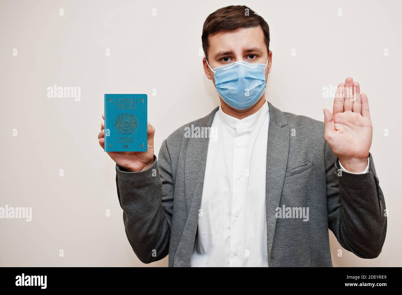 Uomo europeo in abbigliamento formale e maschera facciale, mostrare il passaporto Kazakhstan con la mano del segnale di stop. Blocco del coronavirus nel concetto di paese europeo. Foto Stock