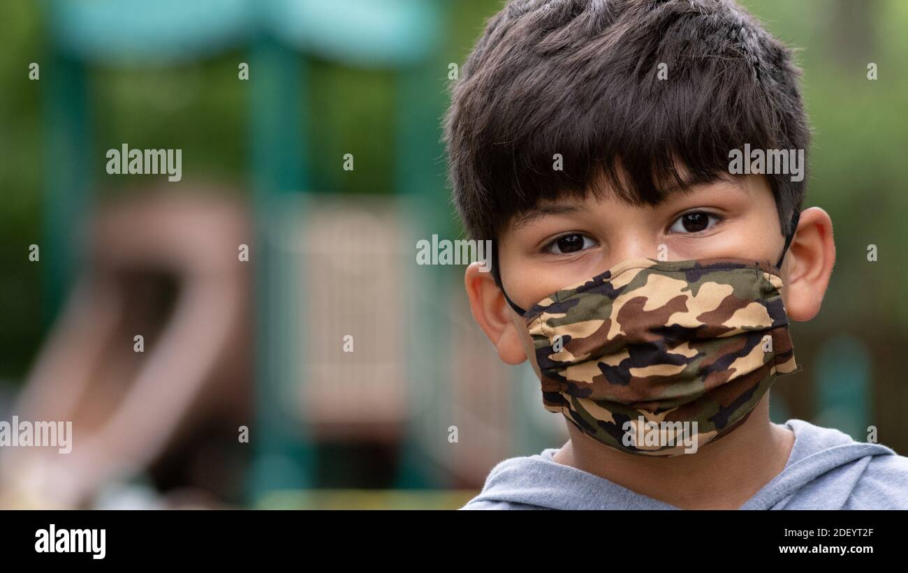 Ragazzo ispanico che indossa una maschera con parco giochi nella parte posteriore durante il Coronavirus covid-19 pandemic distanza sociale, rimanere a casa restrizioni Foto Stock