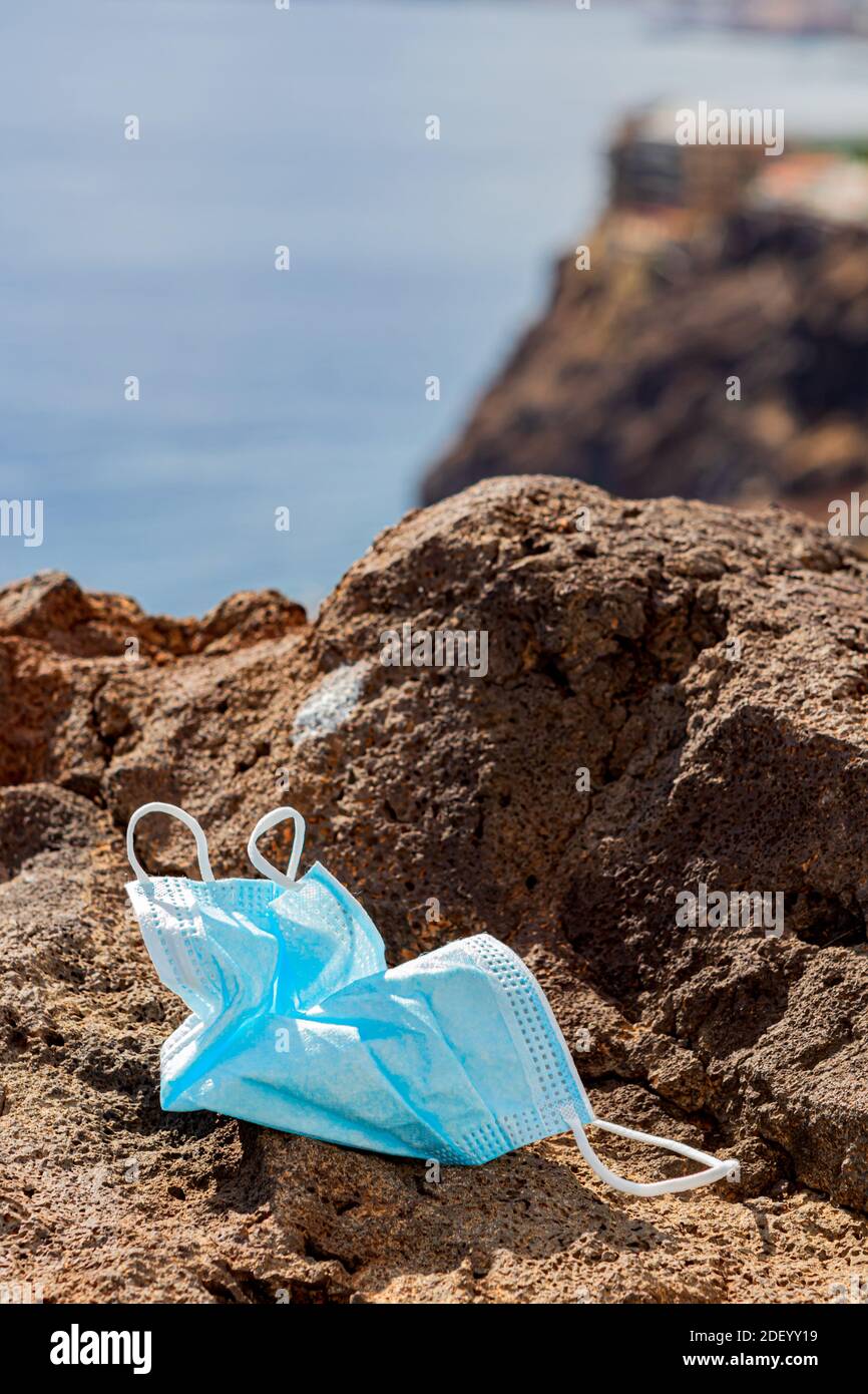Maschera chirurgica gettata via su una roccia di fronte al mare. Primo piano. Verticale Foto Stock