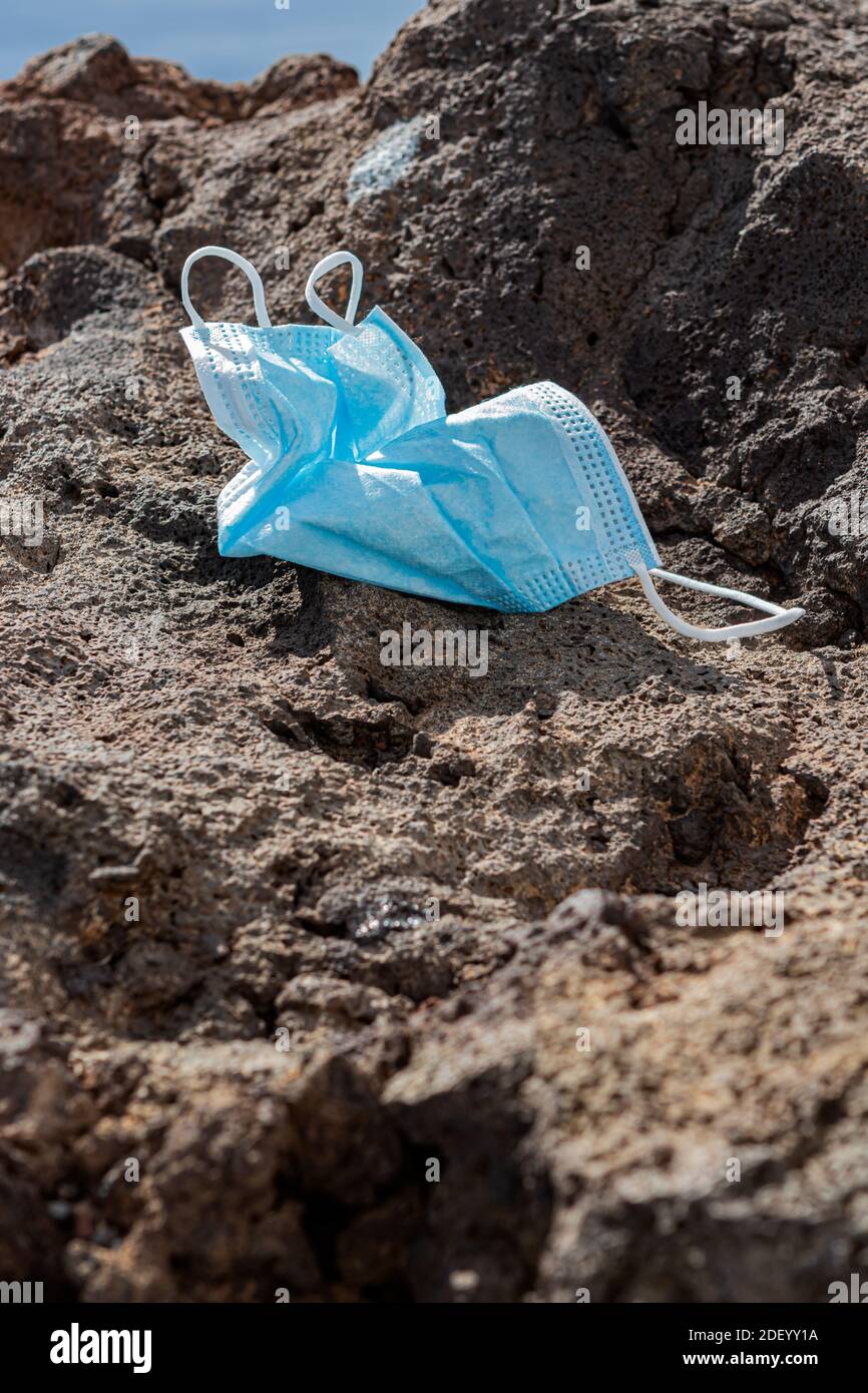 Maschera chirurgica gettata via su una roccia di fronte al mare. Primo piano. Verticale Foto Stock