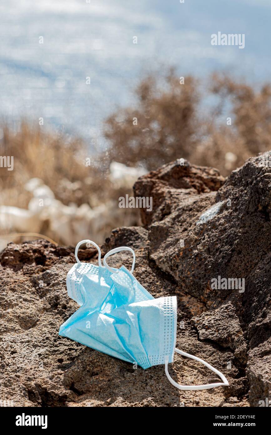 Maschera chirurgica gettata via su una roccia di fronte al mare. Primo piano. Verticale Foto Stock