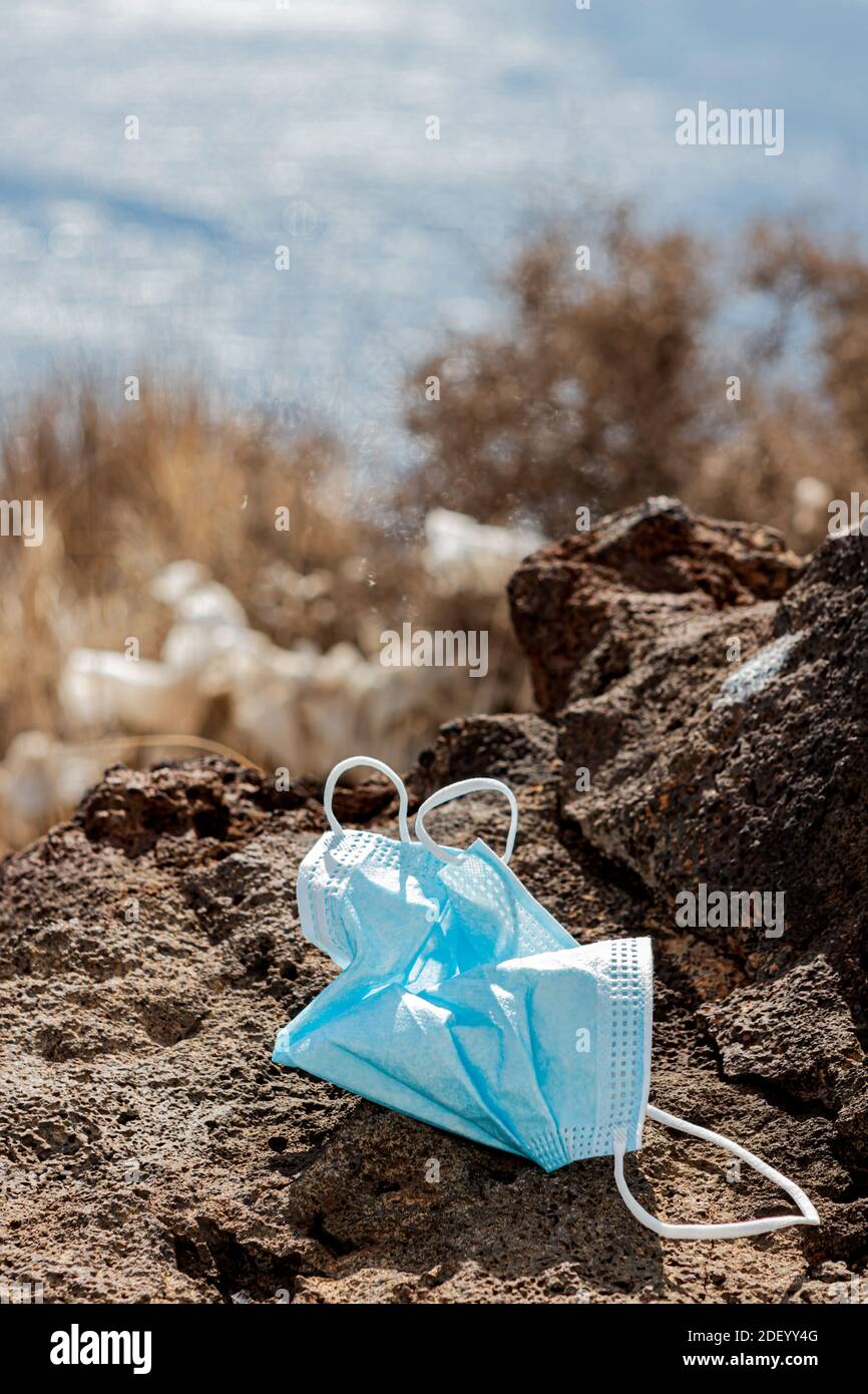 Maschera chirurgica gettata via su una roccia di fronte al mare. Primo piano. Verticale Foto Stock