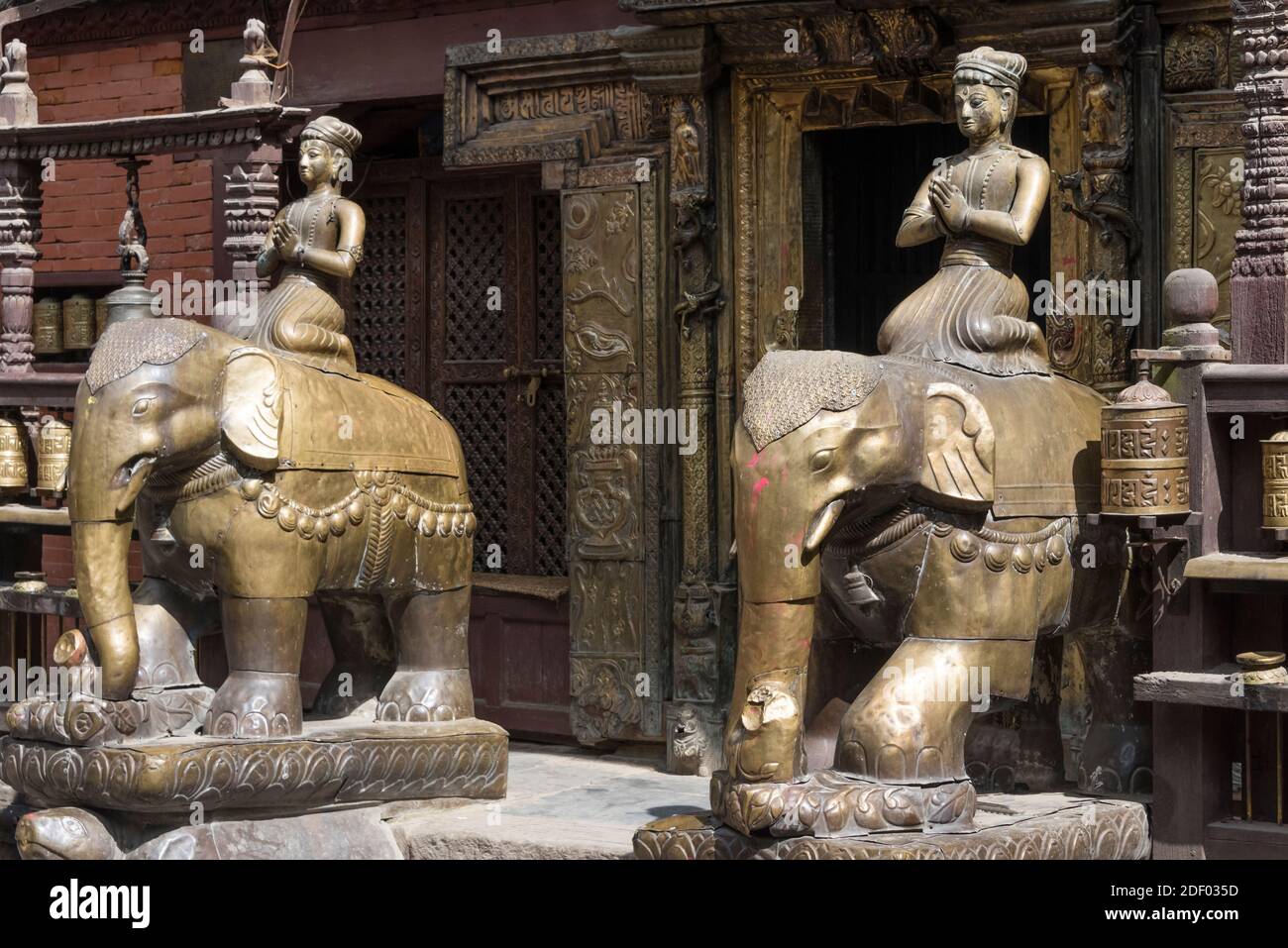 Statua e ruote di preghiera a Hiranya Varna Mahavihar (Kwa Bahal), il Tempio d'oro, Kathmandu, Nepal Foto Stock