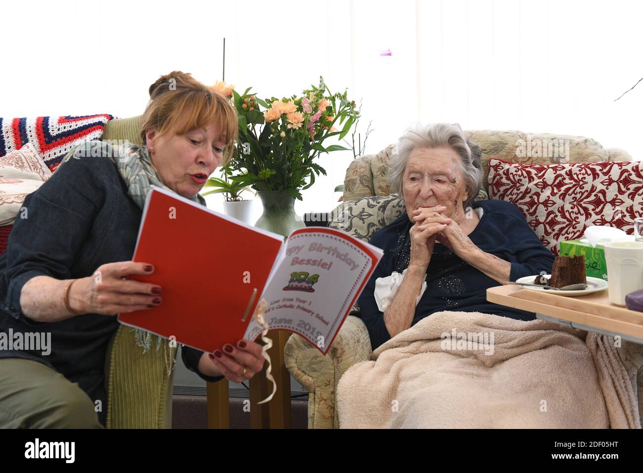 Donna che legge alla sua madre anziana che celebra il suo 104th compleanno in casa di cura Gran Bretagna, Regno Unito. Foto Stock