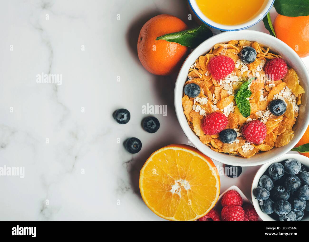 Colazione sana. Ciotola con cereali, lamponi, mirtilli, mandarini e succo d'arancia su tavola di marmo Foto Stock