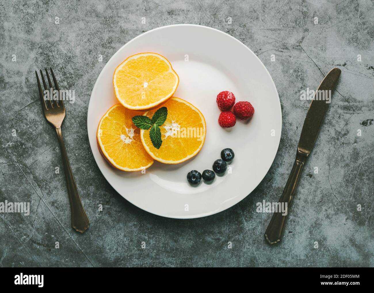 Dessert sano. Piatto bianco con fette di arancia, lamponi, mirtilli e antiche posate d'annata su sfondo grunge Foto Stock