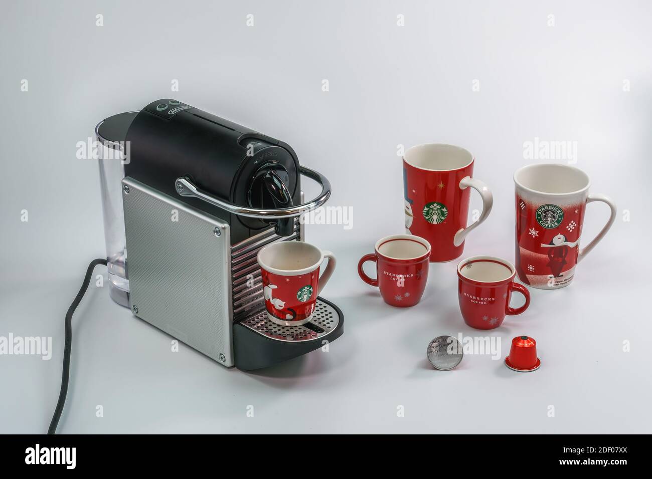 Caffè Starbucks, tazze da caffè di Natale accanto alla macchina Nespresso.  Varietà di tazze di marca per le vacanze dietro le capsule di alluminio  utilizzate per preparare le bevande Foto stock 