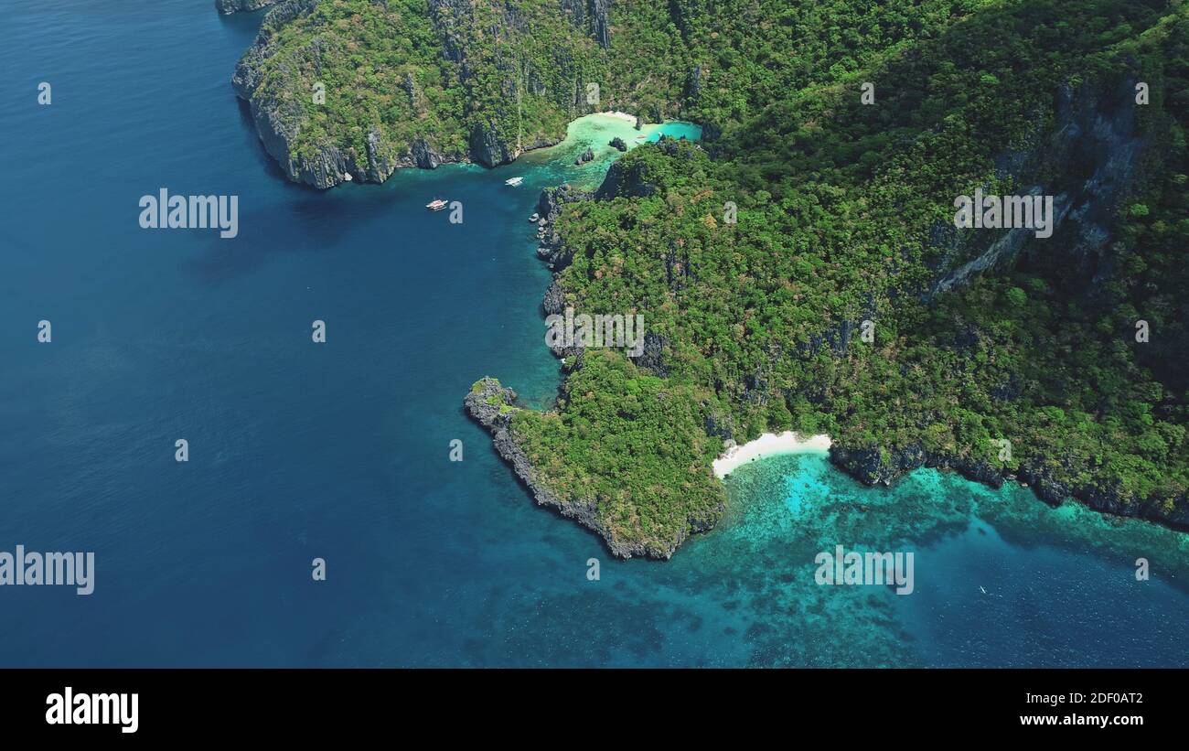 In cima alla verde isola montagnosa sulla baia dell'oceano in vista aerea. Piccole imbarcazioni da passeggeri a mare costa. Paesaggio naturale tropicale con spiaggia di sabbia bianca dell'isola di Palawan, Filippine, Asia Foto Stock