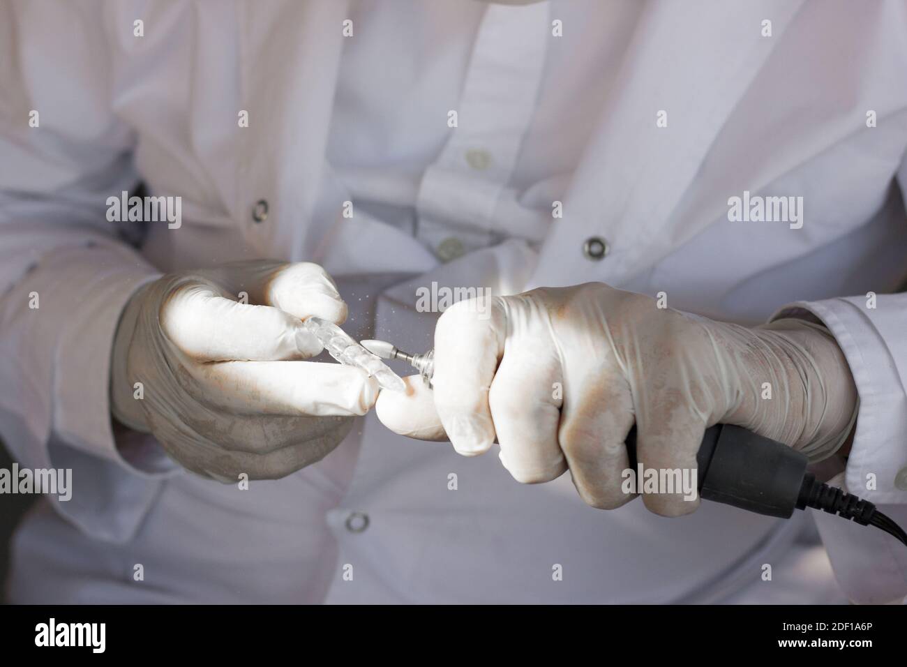Primo piano sulle mani del dentista coperte con guanti in lattice sagomati protezione per bocca con lima Foto Stock