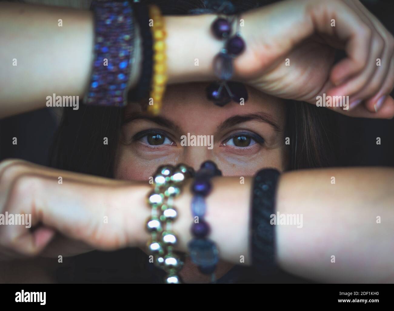 donna adulta guardando la fotocamera nascondendo il viso dietro le braccia con bracciali Foto Stock