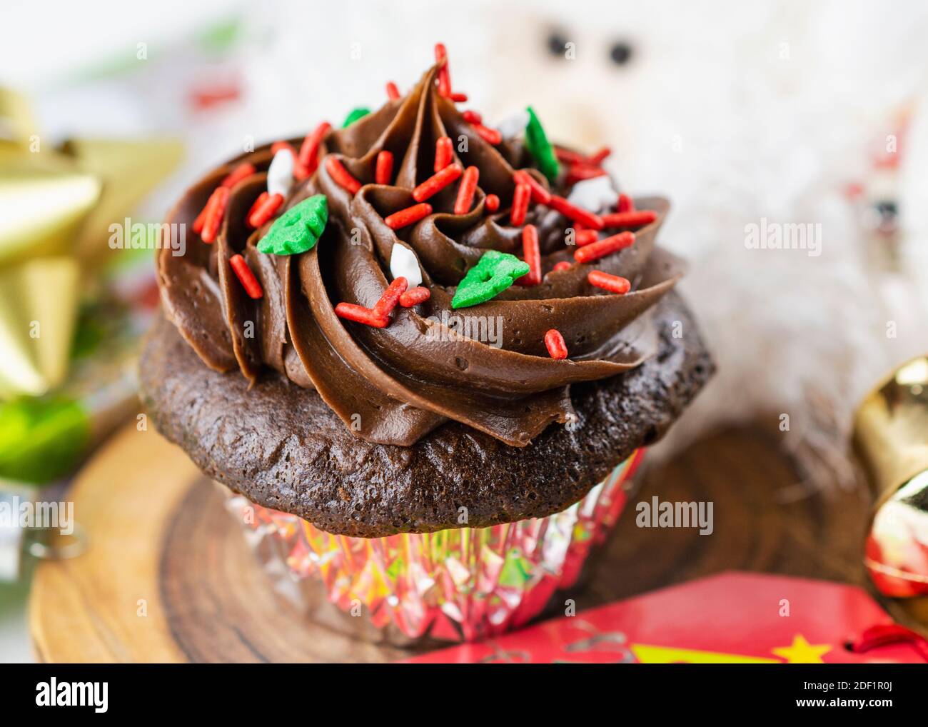 Un cupcake di Natale di cioccolato si siede su un tavolo circondato da etichetta regalo, archi, ornamenti e una Santa. Foto Stock