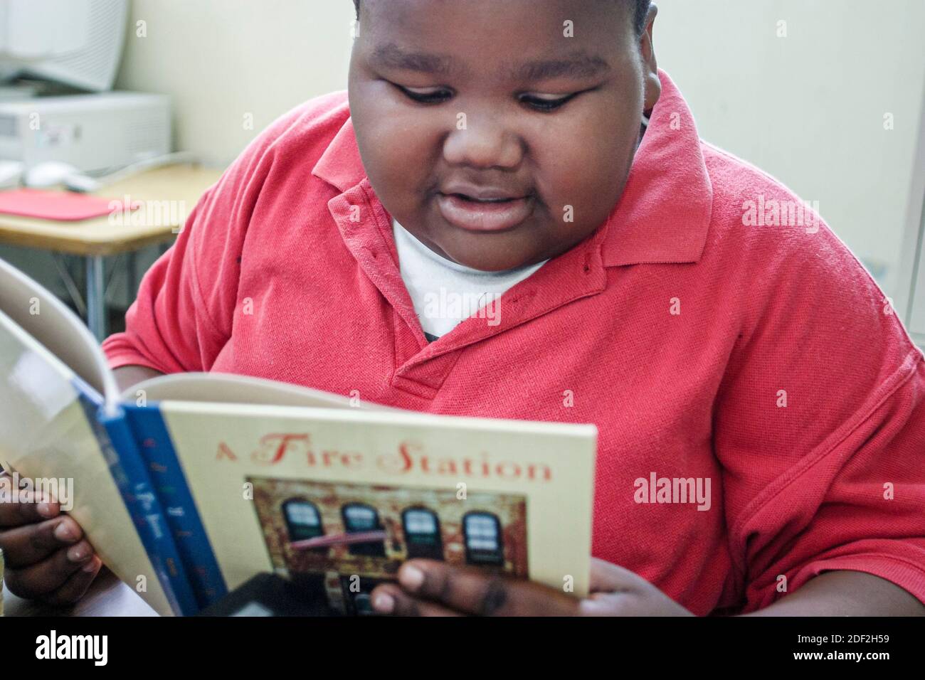 Miami Florida,Little Haiti Edison Park Elementary School,sovrappeso obeso grasso africano nero ragazzo studente, legge lettura, Foto Stock