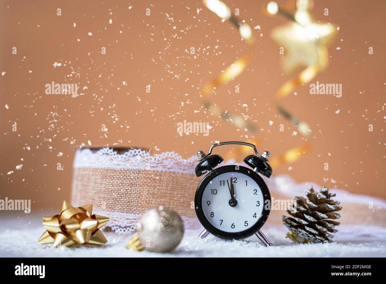 Sveglia, giocattoli dell'albero di Natale e cono di pino su sfondo beige con neve. Decorazioni natalizie, concetto di Capodanno. Profondità di campo poco profonda. Foto Stock