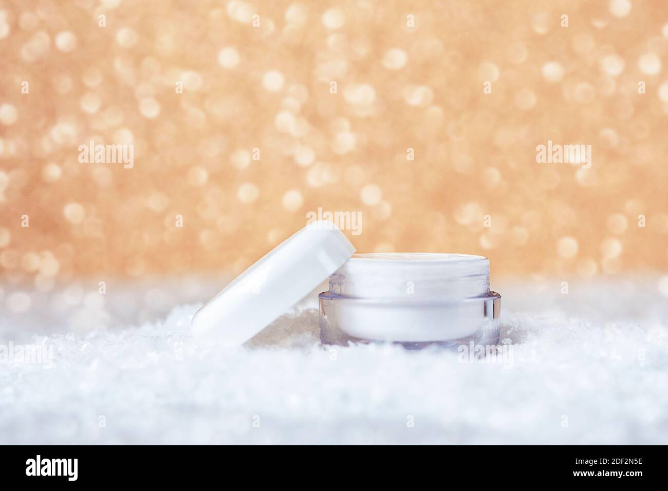 Crema cosmetica in vaso bianco per la cura della pelle del viso e delle mani. Sfondo bokeh dorato. Concetto di cura della pelle invernale. Foto Stock