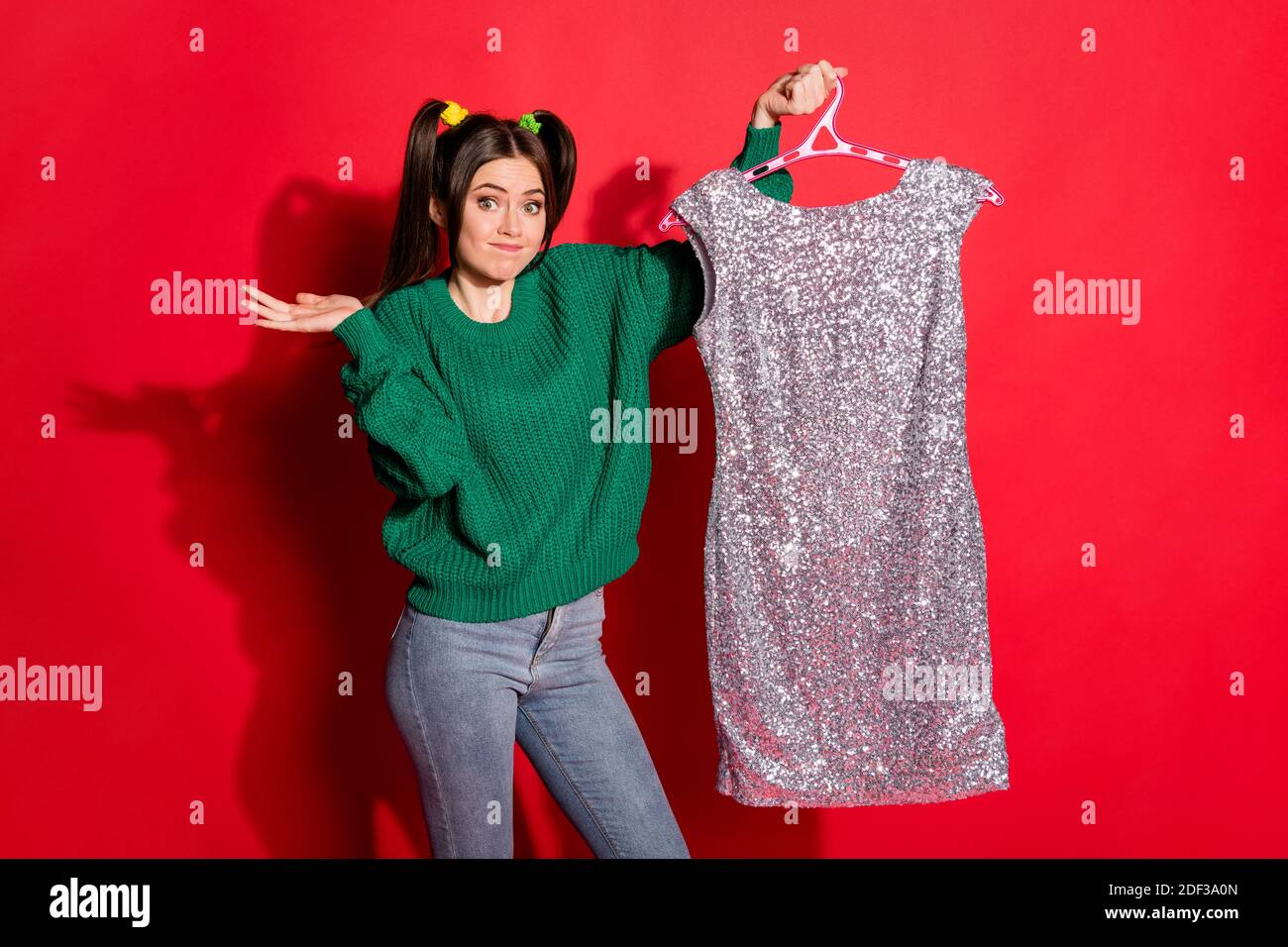 Foto di una giovane donna bella incerta indossare un pullover a maglia verde scegli nuovo abito isolato rosso colore sfondo Foto Stock