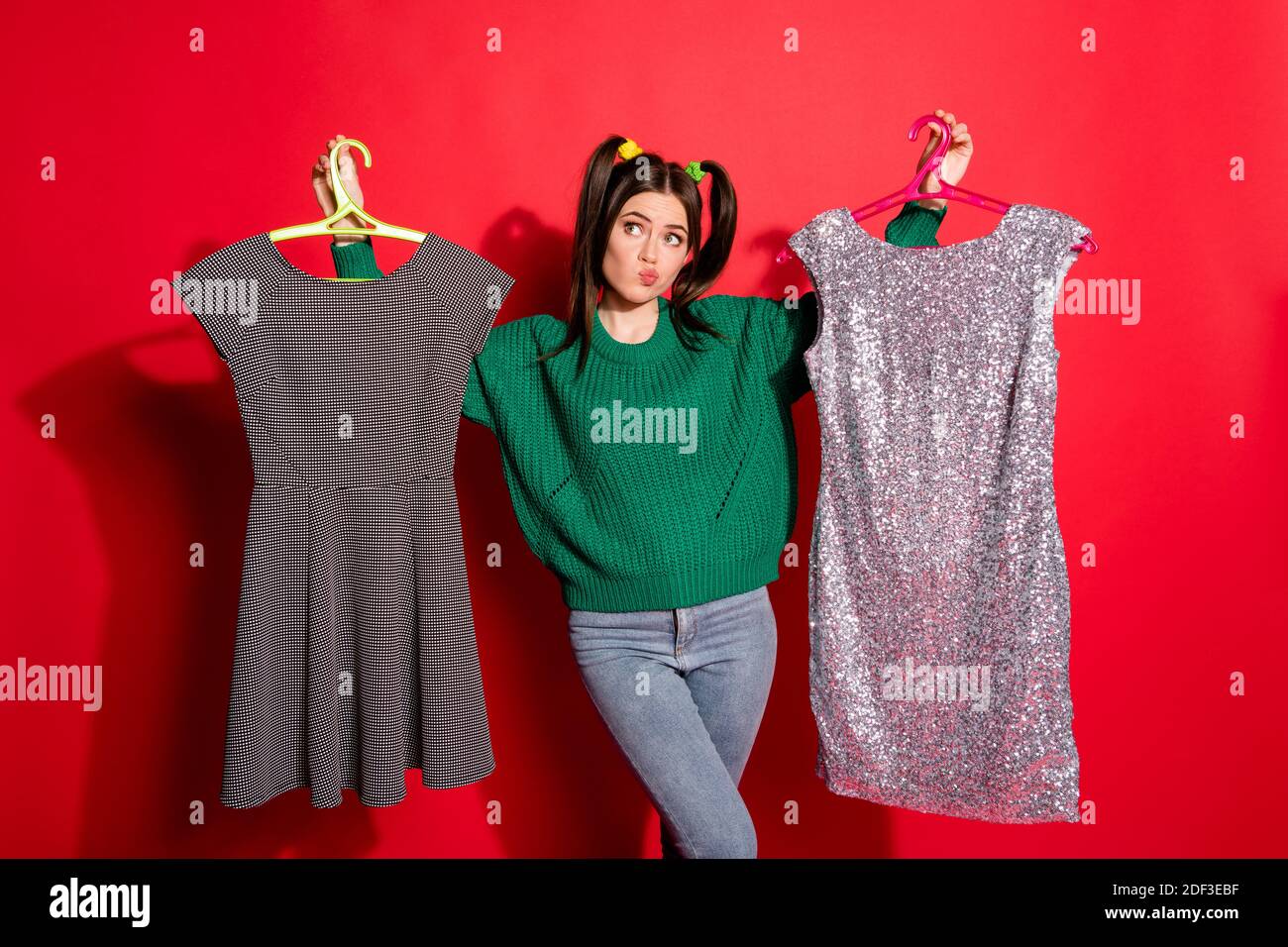 Foto di carino donna incerta giovane vestito verde maglia maglione prova a scegliere l'abito per data isolato di colore rosso sfondo Foto Stock