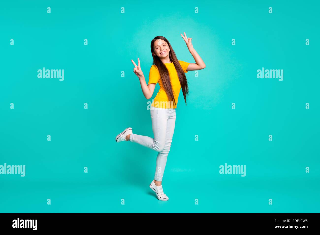 Foto a dimensione intera di ragazza allegra di capretto fare V-segno in piedi isolato su sfondo di colore turchese Foto Stock