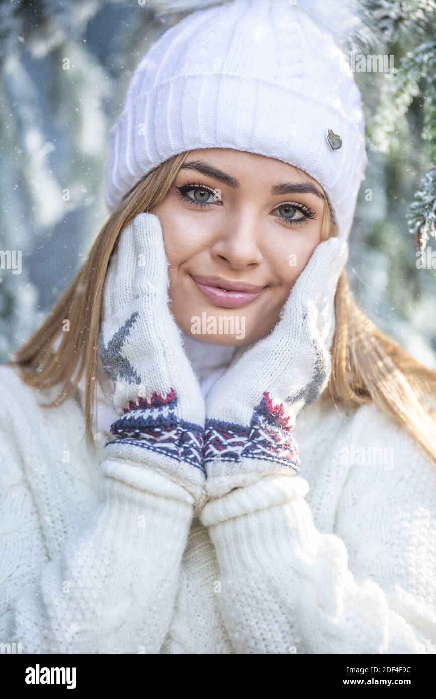 Una ragazza dall'aspetto elegante tocca la pelle morbida del viso con guanti invernali, vestita con un maglione e un'api. Foto Stock