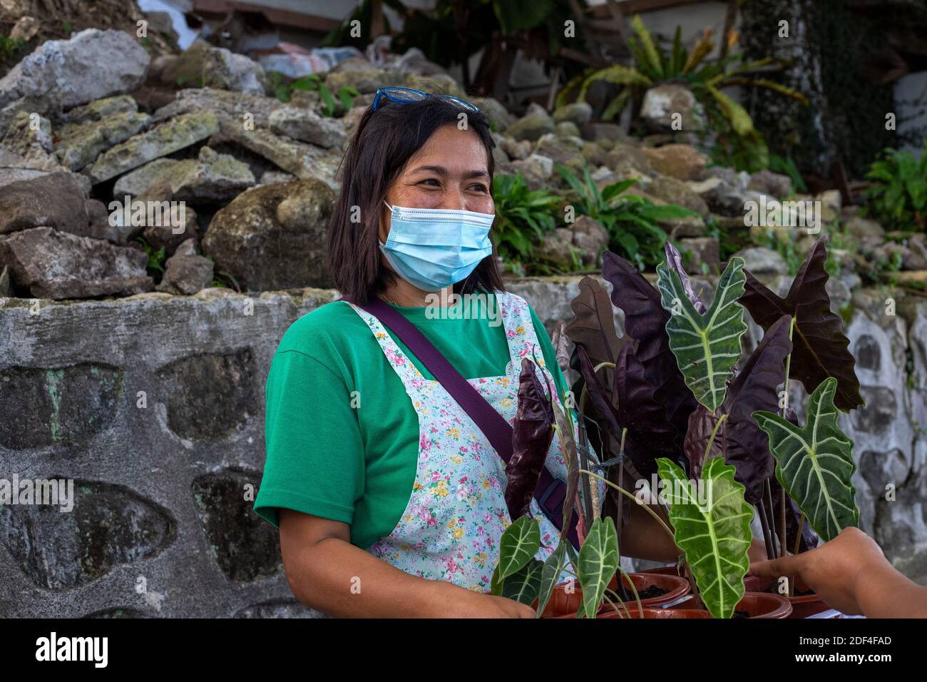 Dumaguete, le Filippine - 28 novembre 2020: Donna in maschera di faccia che vende fiori . Friendly Filippina in maschera protettiva sul mercato. Mercato agricolo nuovo normale Foto Stock
