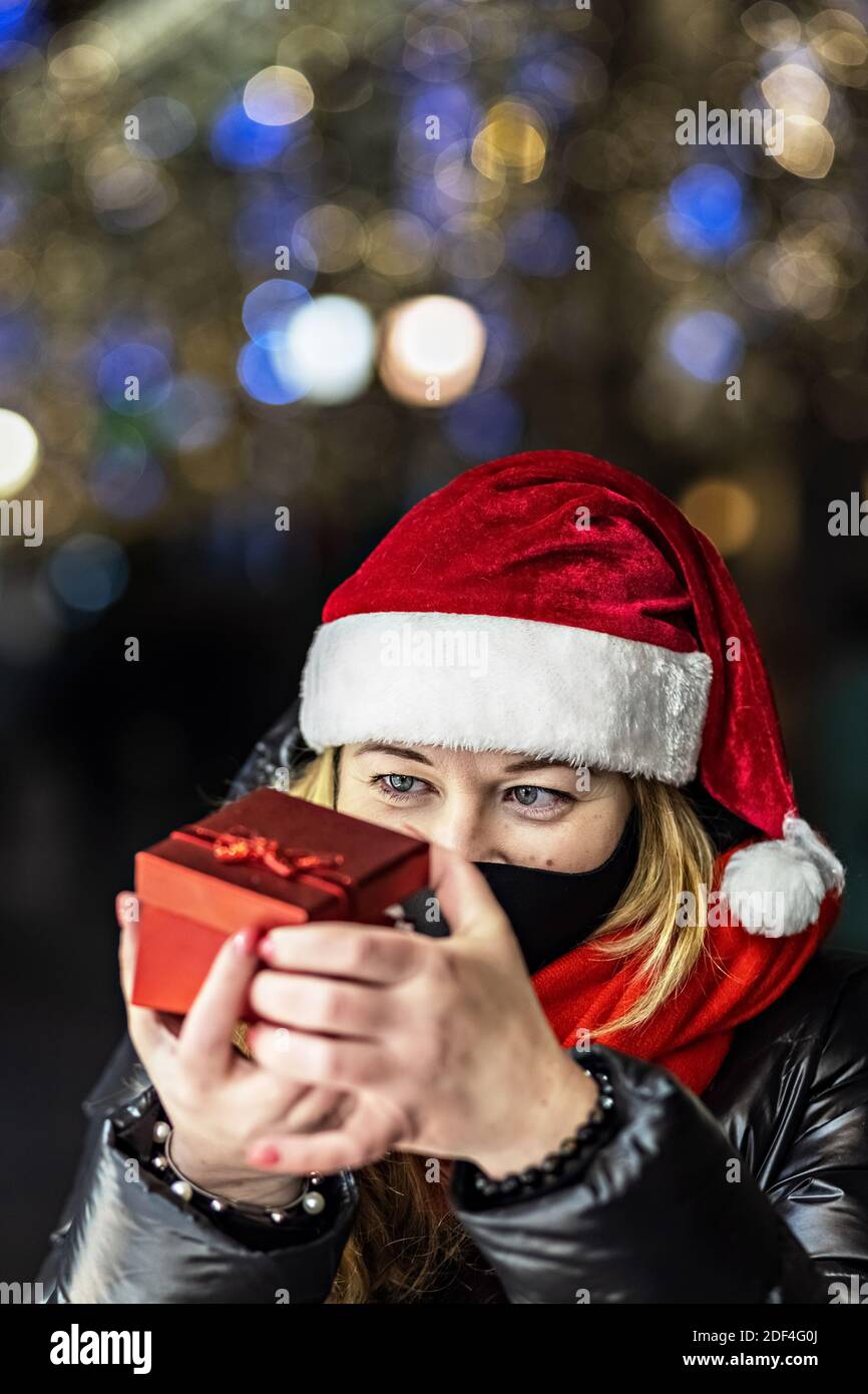 Una donna in un cappello di Santa apre una scatola regalo rossa festiva. Vacanze di Natale. Foto Stock