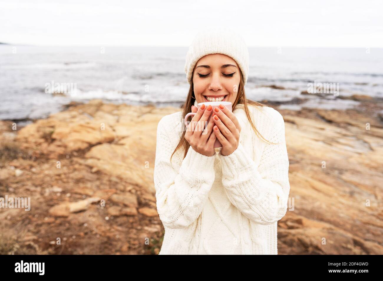 Giovane donna caucasica tiene una tazza di tè in lei mani con gli occhi chiusi anticipando il calore del Drink all'aperto in freddo clima invernale - Sing Foto Stock