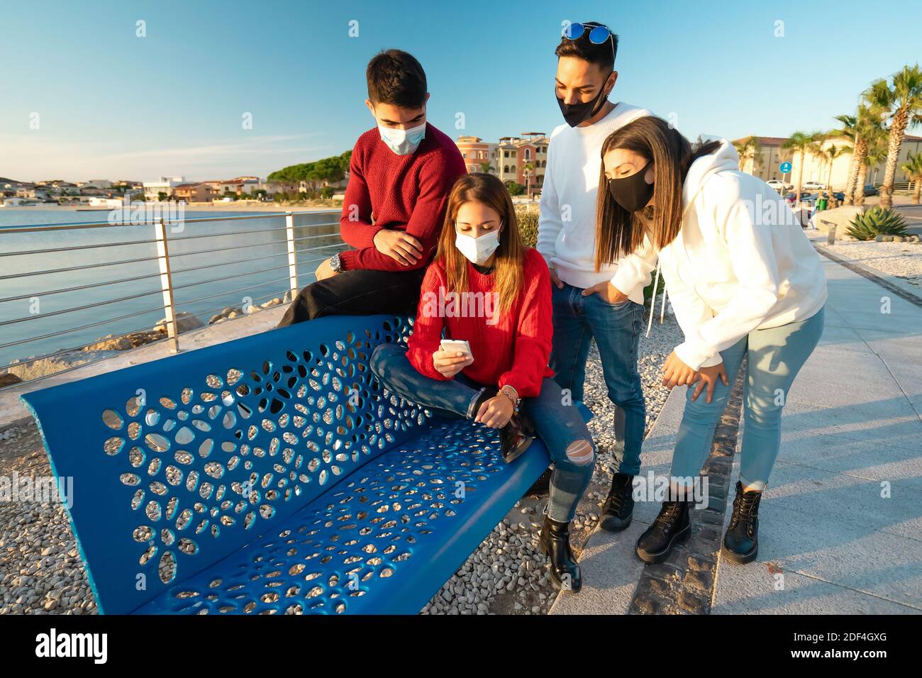 Due coppie eterosessuali caucasiche in rosso e bianco pullover in cerca Presso lo smartphone in vacanza invernale - Gruppo di amici che indossano la protezione Foto Stock